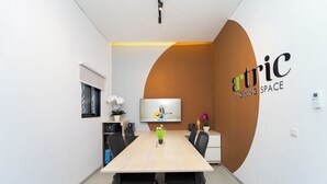 A modern conference room with a long table, black office chairs, a television, and a logo on the wall. - Artric Profesional Living by ARBA (Semarang)