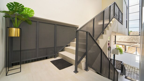 A modern staircase with metal railings, a potted plant, and a view of the outside. - Artric Profesional Living by ARBA (Semarang)