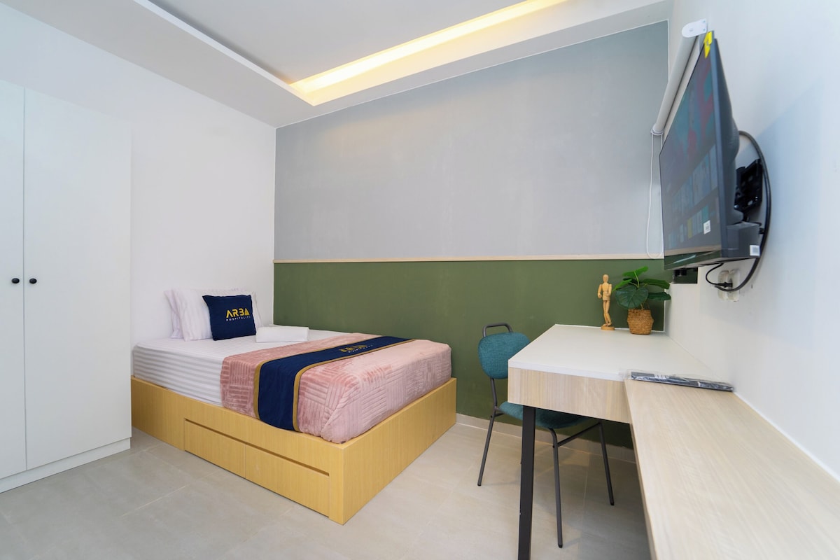 A modern bedroom with a bed, a desk, and a television mounted on the wall.