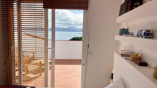 Un dormitorio con una cama, vistas al mar y una estantería con libros y un coche de juguete.