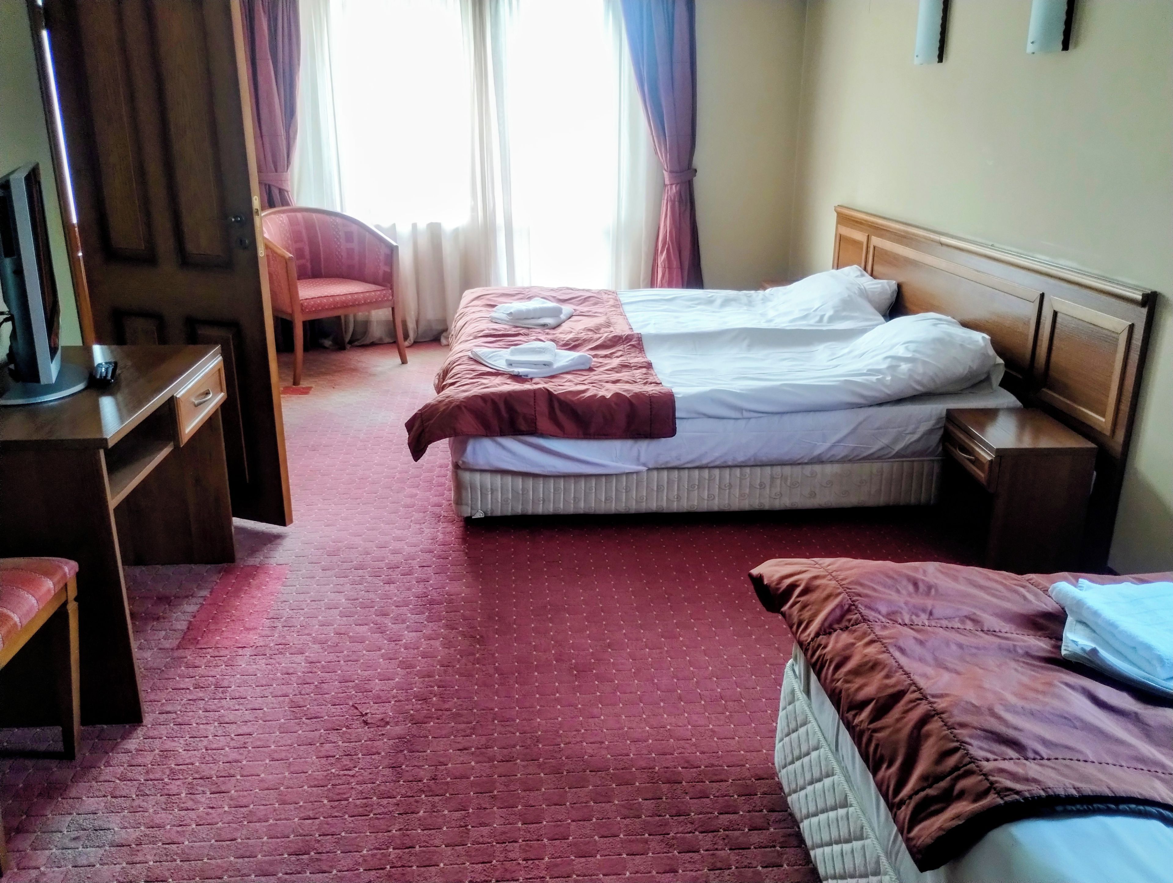 Hotellihuone, jossa on kaksi sänkyä, työpöytä, tuoli ja ikkuna, jossa on verhot.