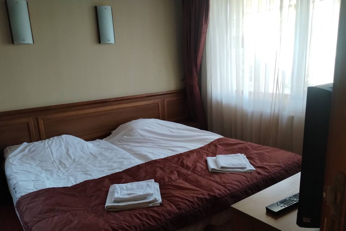 A hotel room with a bed, a TV, and a window with curtains.