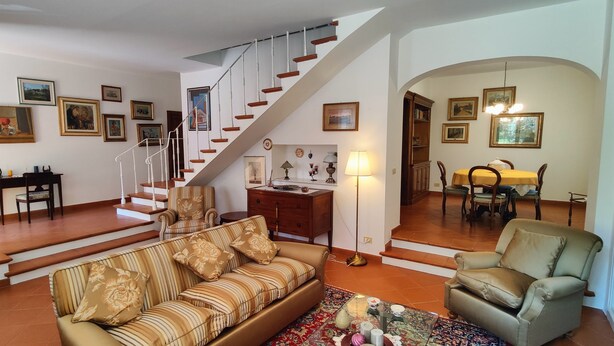 Una sala de estar con una escalera, una zona de comedor y una estantería.