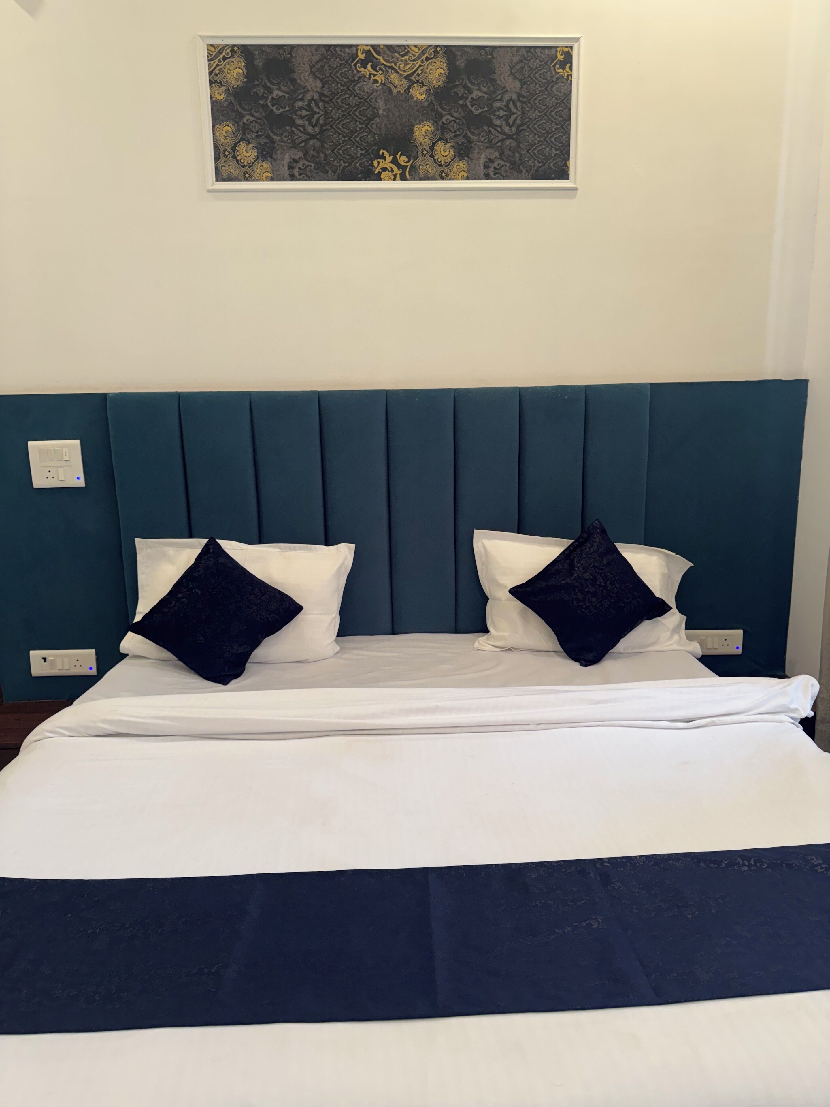 A neatly made bed with a teal headboard, white bedding, and two dark blue pillows.