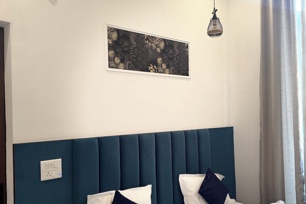 A bedroom with a bed, two bedside tables, a wall-mounted light fixture, a power outlet, and a window with curtains.