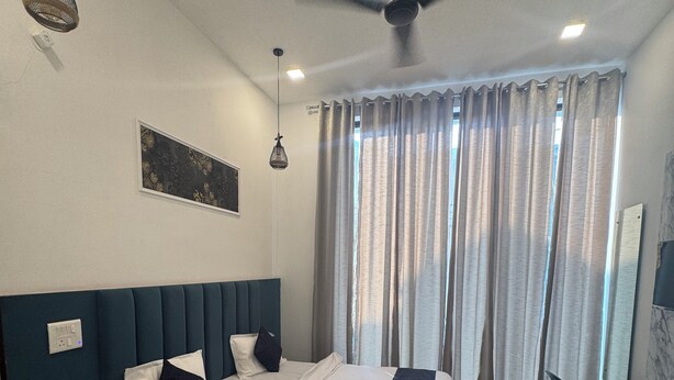 A hotel room with a large bed, a ceiling fan, a desk, and a window with curtains. - Jasmin A Luxury Stay (Agra)