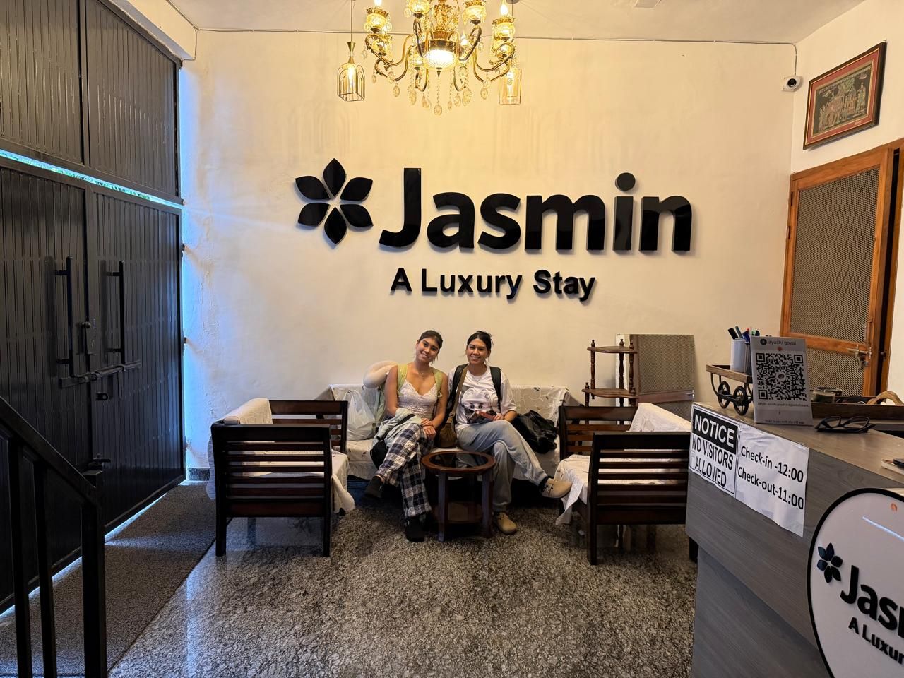 Un espace d’accueil avec une enseigne indiquant « Jasmin, un séjour de luxe », un lustre et un panneau d’affichage indiquant les heures d’arrivée et de départ.