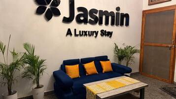 Zona de recepción con un sofá azul, dos plantas en macetas y un cartel que dice 'Jasmin A Luxury Stay'.