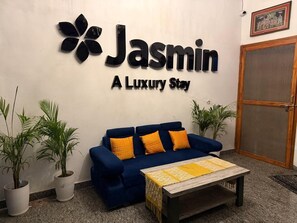 A reception area with a blue sofa, two potted plants, and a sign that reads 'Jasmin A Luxury Stay'. - Jasmin A Luxury Stay (Agra)