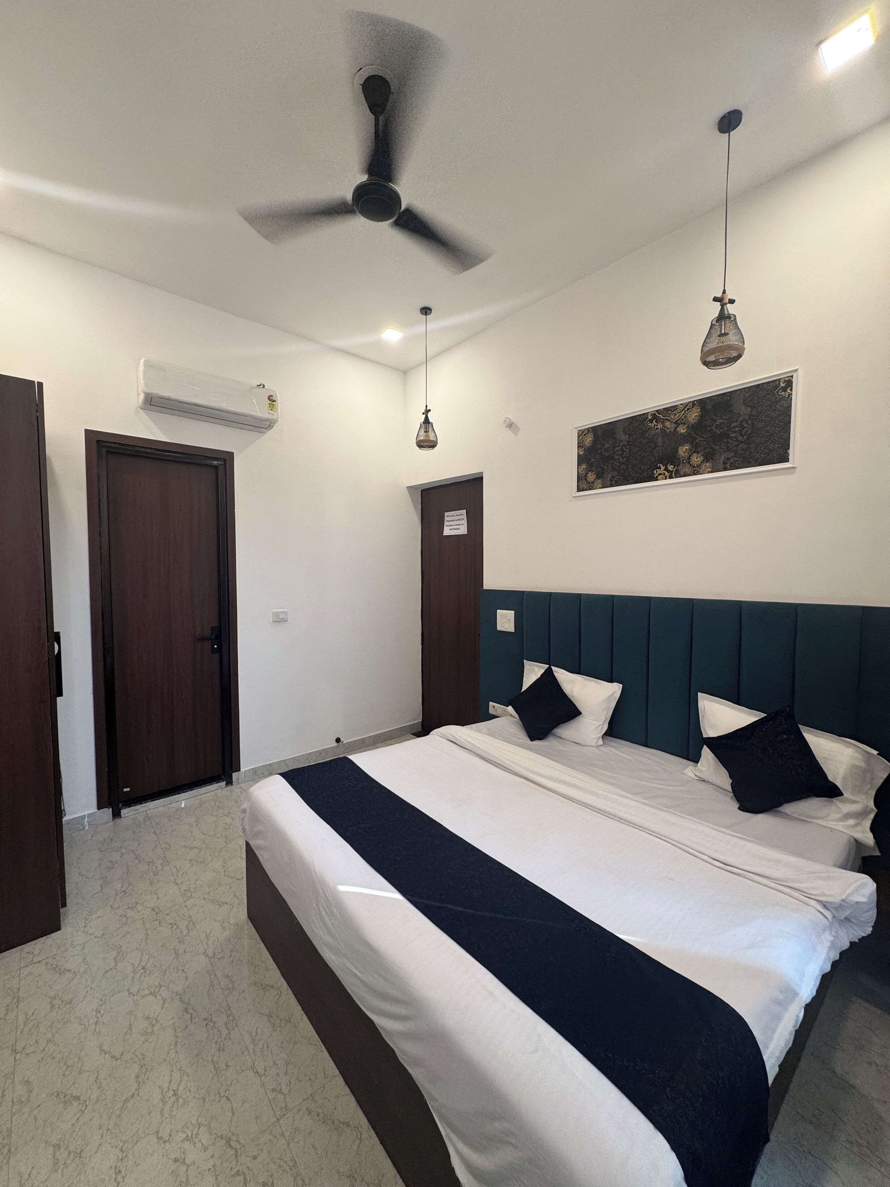 Una habitación de hotel con cama, ventilador de techo, aire acondicionado y un cuadro en la pared.