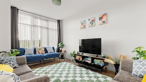 A living room with a blue sofa, a grey armchair, a TV, and a bookshelf. - Hartley Avenue (Leeds)