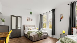 A bedroom with a bed, a desk, a chair, a wardrobe, a window, and a bedside table. - Hartley Avenue (Leeds)