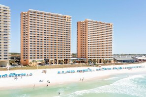 A beachfront hotel with multiple high-rise buildings, a sandy beach, and a clear sky. - Sand-Toes Living | Gulf-Front, Walk to Pier Park (Panama City Beach)