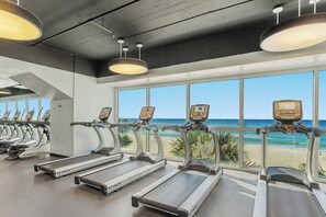 A gym with treadmills, large windows, and a view of the beach. - Sand-Toes Living | Gulf-Front, Walk to Pier Park (Panama City Beach)