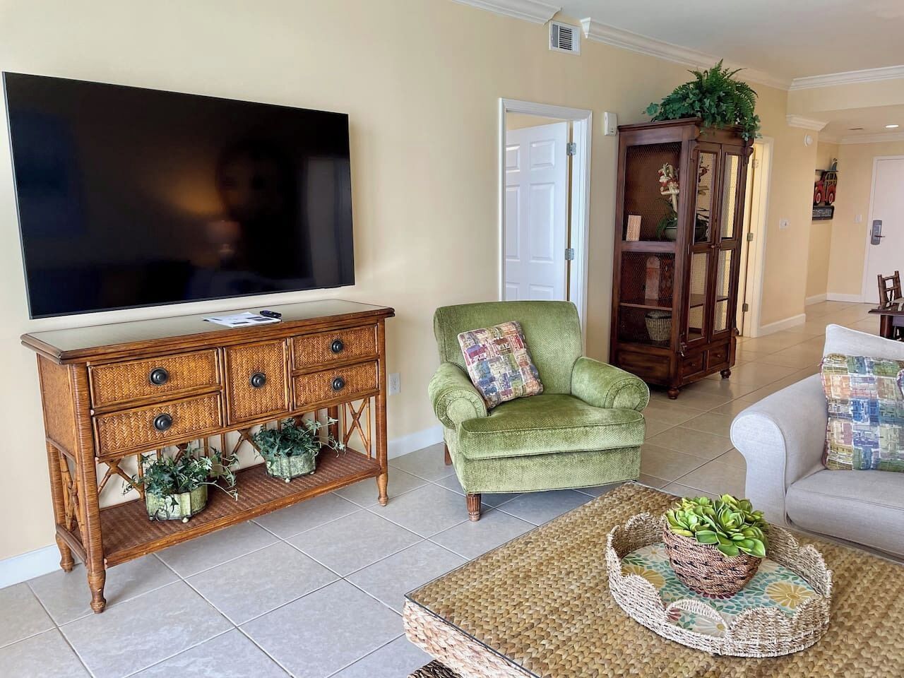 Una sala de estar con una televisión, un sillón verde, un aparador de madera y un sofá blanco.