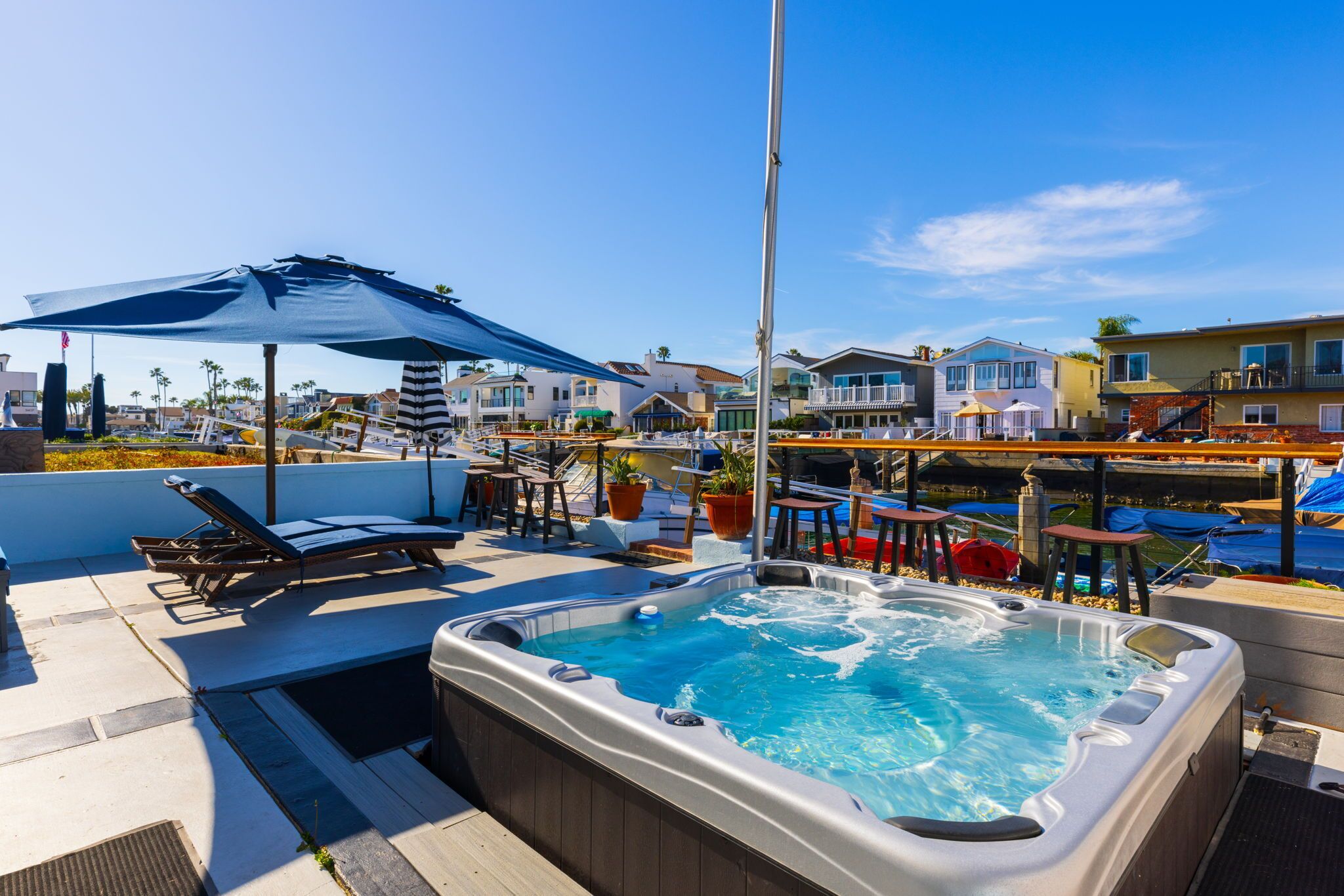A rooftop pool area with lounge chairs, a hot tub, and a view of surrounding houses.