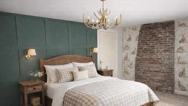 A bedroom with a wooden bed, green walls, a brick fireplace, and wall-mounted lamps. - The Huntsman (Strumpshaw)