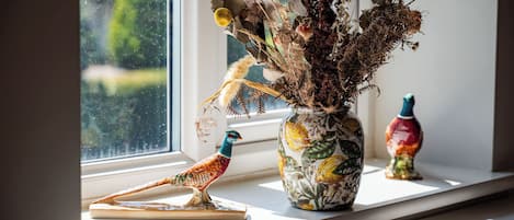 Un alféizar con un jarrón decorativo, una figurita de pájaro y una botella de colores.