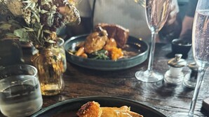 A dining table with plates of food, glasses of water, and a vase with dried flowers. - The Huntsman (Strumpshaw)