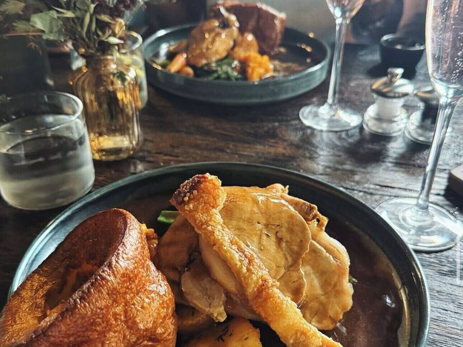 A dining table with plates of food, glasses of water, and a vase with dried flowers.