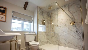 A bathroom with a marble shower wall, a toilet, a sink, and a window. - The Huntsman (Strumpshaw)