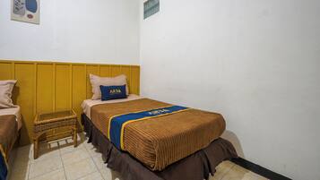 A small, simple room with two beds, a small table, and a wall-mounted shelf.