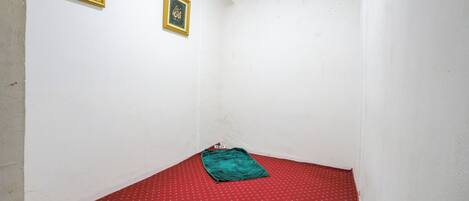A small room with a red patterned carpet, two framed calligraphy pieces on the wall, and a green blanket on the floor.