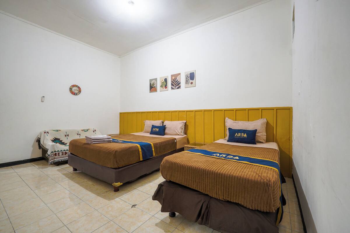 A hotel room with two beds, a yellow headboard, and a small couch.