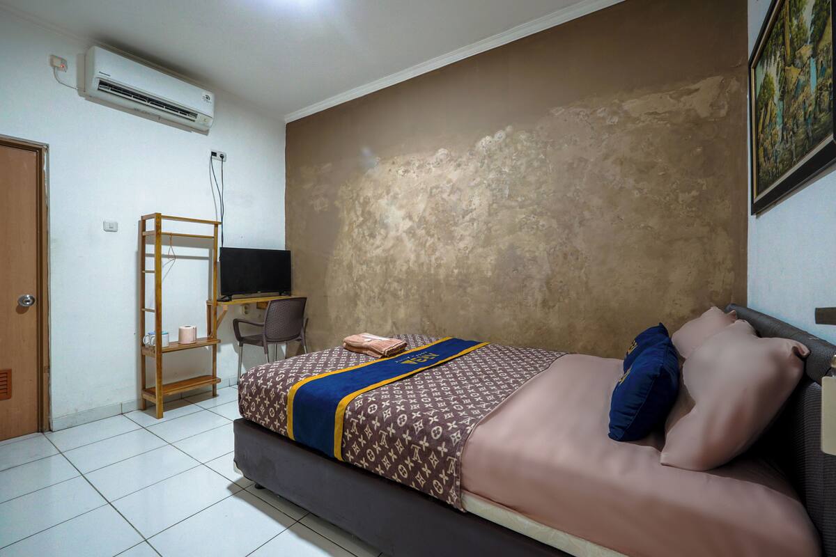 A bedroom with a bed, a desk, a chair, and an air conditioning unit.