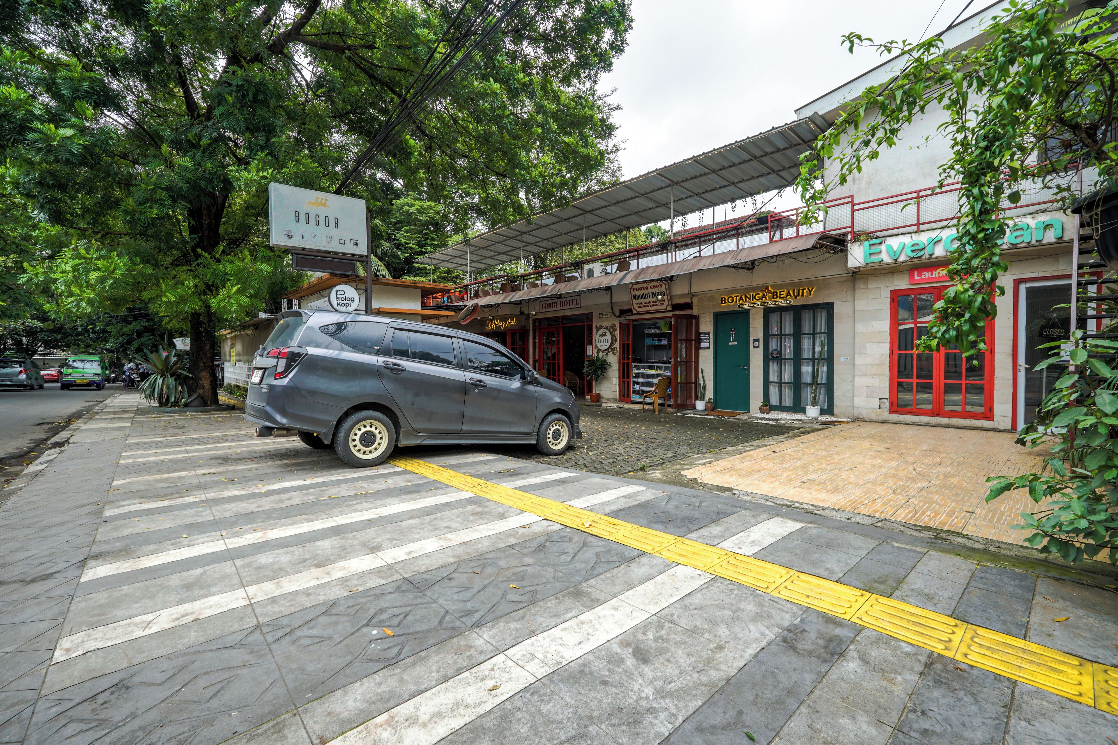 A parking area with a car, a building with a sign reading "Evergreen," and a tree in the background.