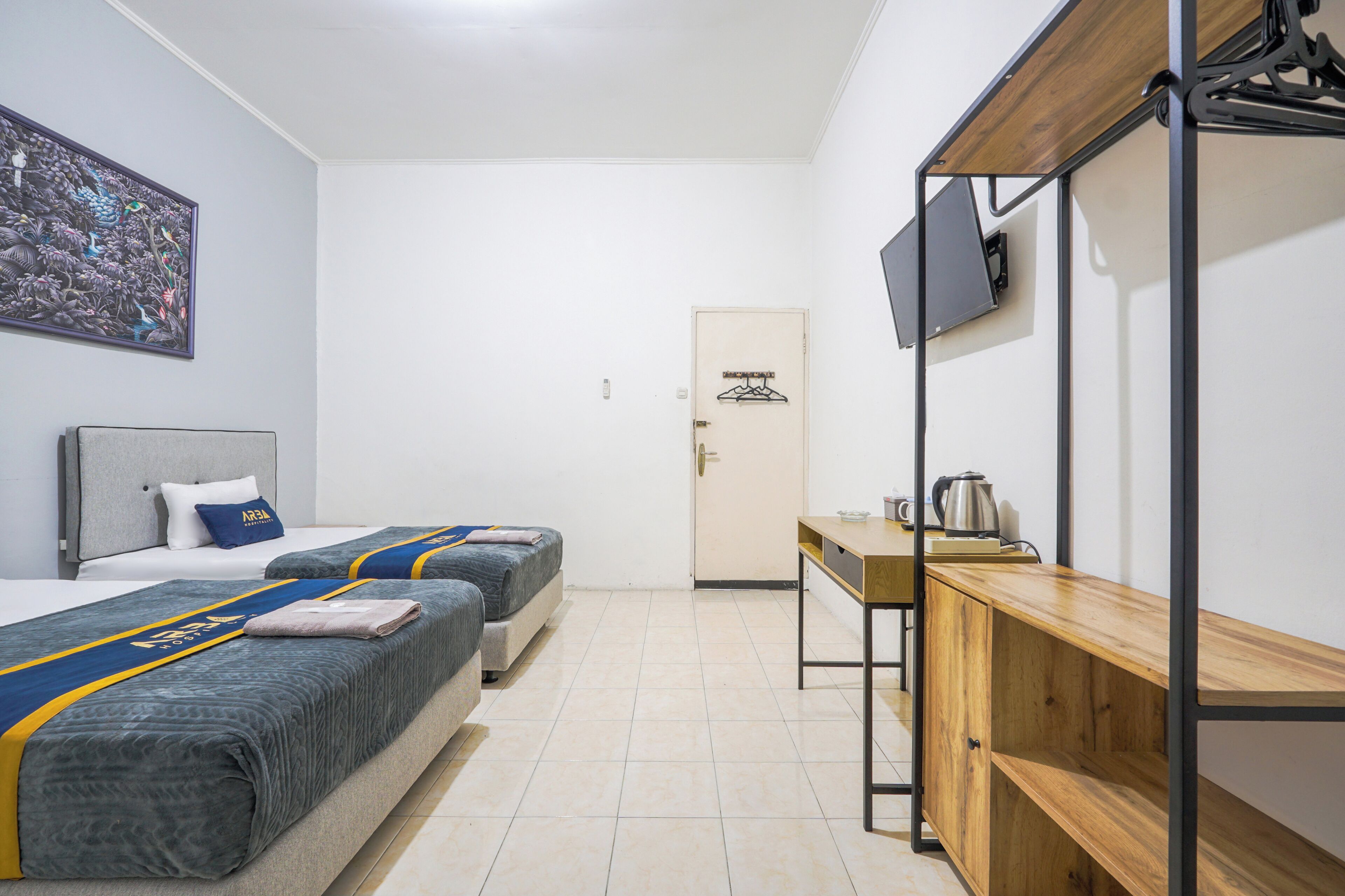 Ein Hotelzimmer mit zwei Betten, einem Schreibtisch, einem Fernseher und einer Tür mit Kleiderhaken.