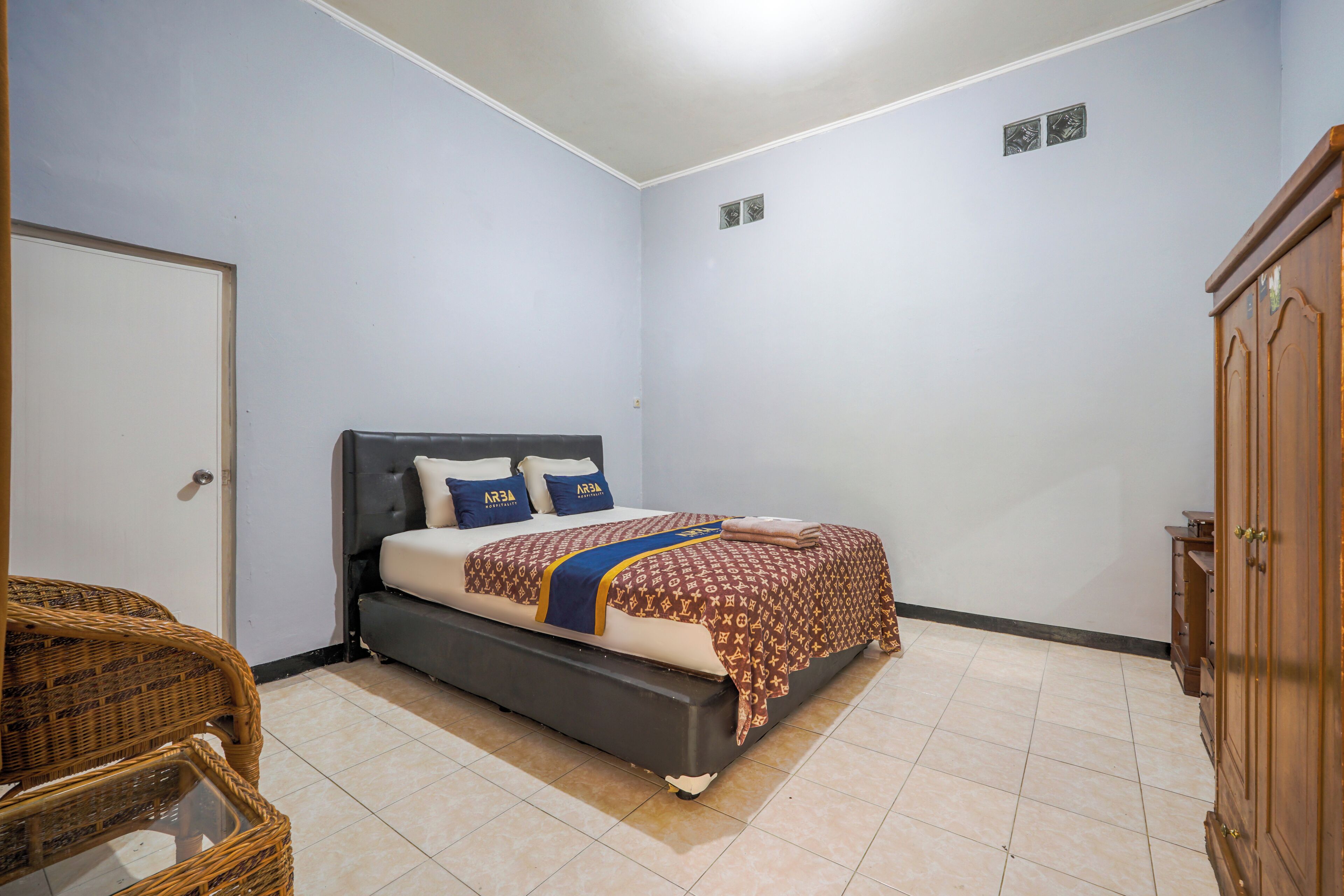 Un dormitorio con cama, armario y una silla de mimbre.