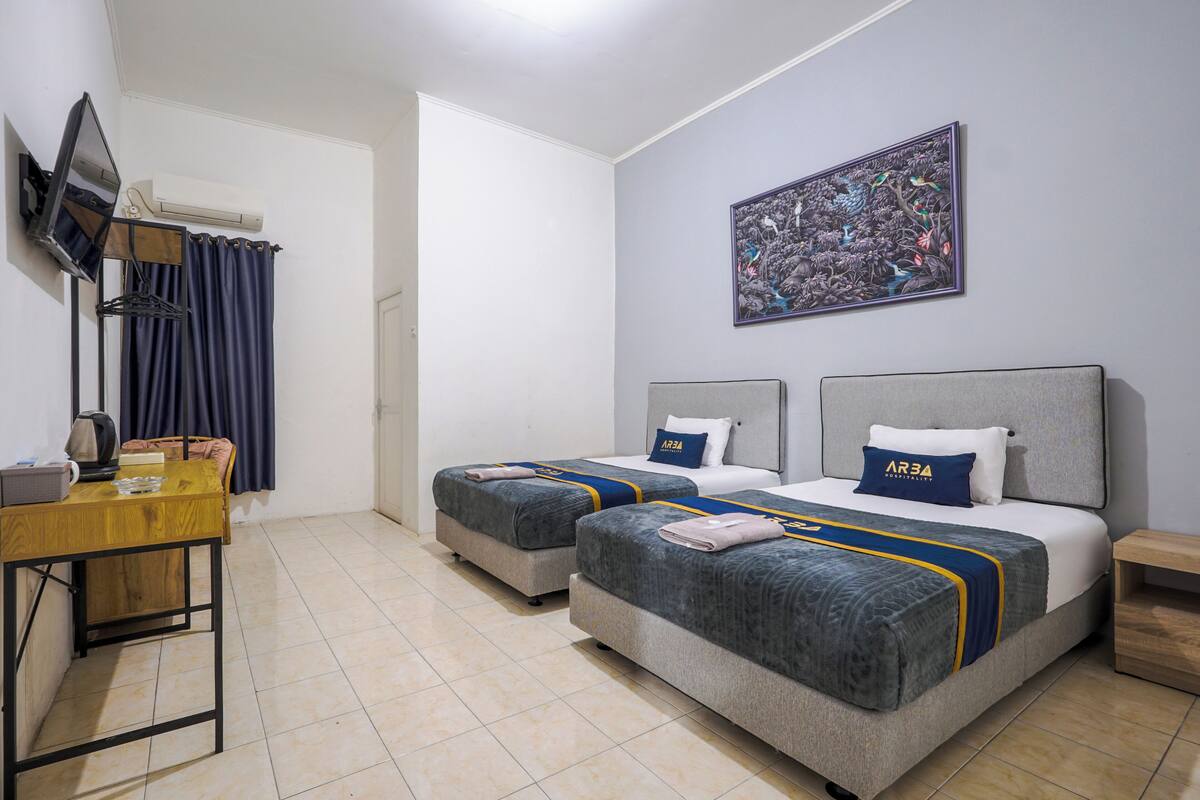 A hotel room with two beds, a desk, a TV, and a painting on the wall.