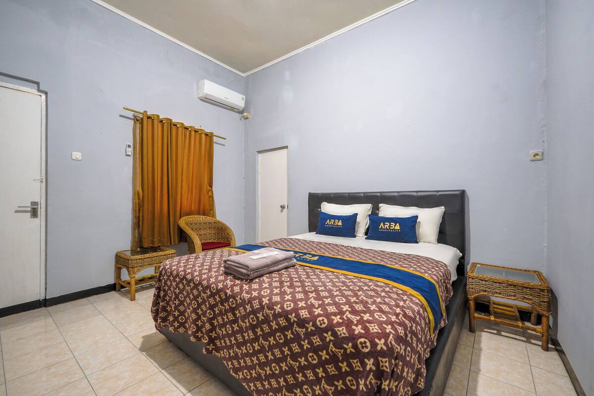 A bedroom with a bed, a chair, a small table, and an air conditioning unit.