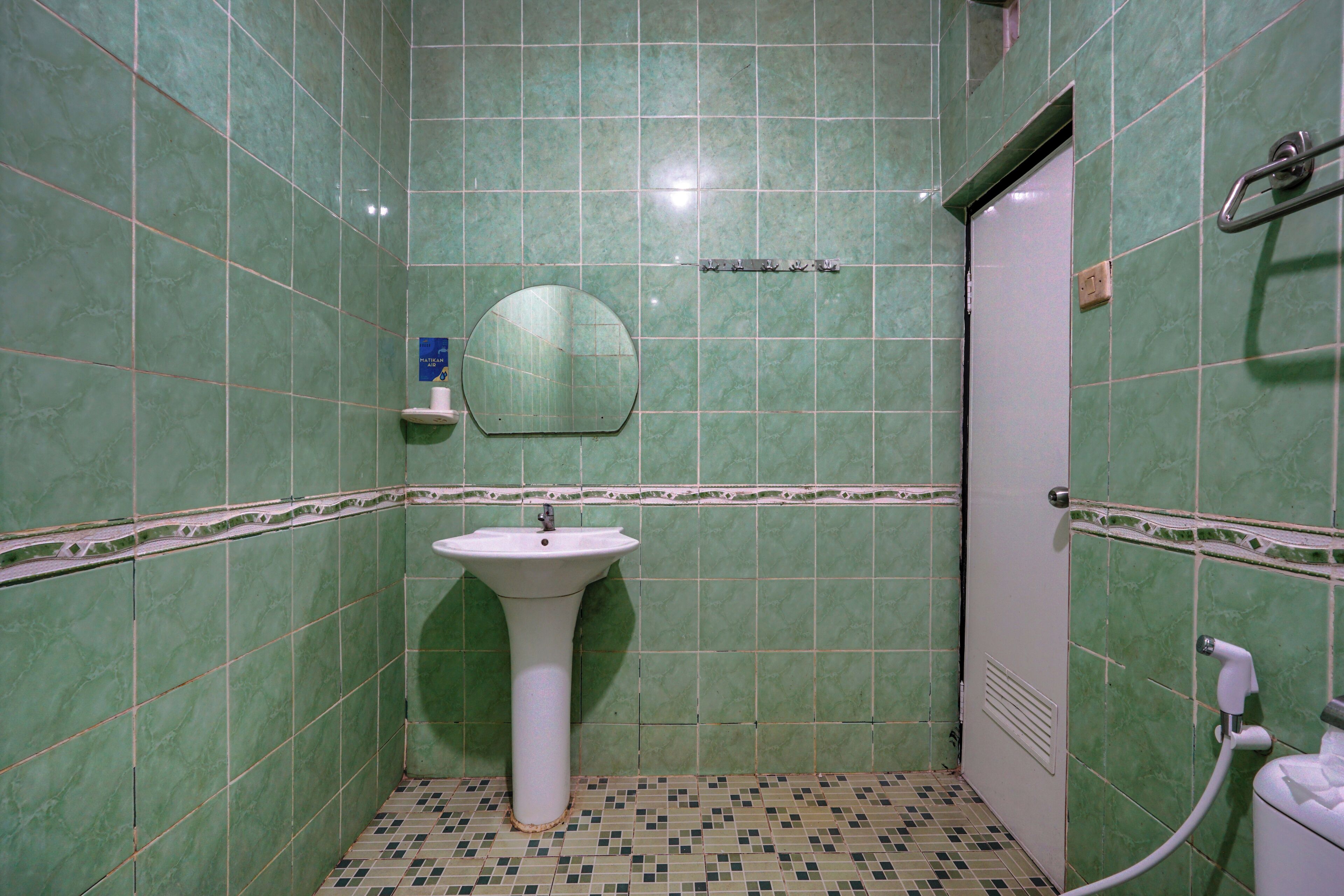 Un baño con azulejos verdes, un lavabo blanco, un espejo y una zona de ducha.