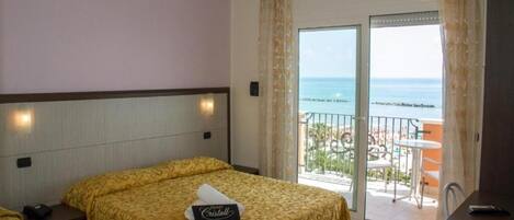 Habitación de hotel con dos camas, un balcón con vista al mar y una pequeña mesa.