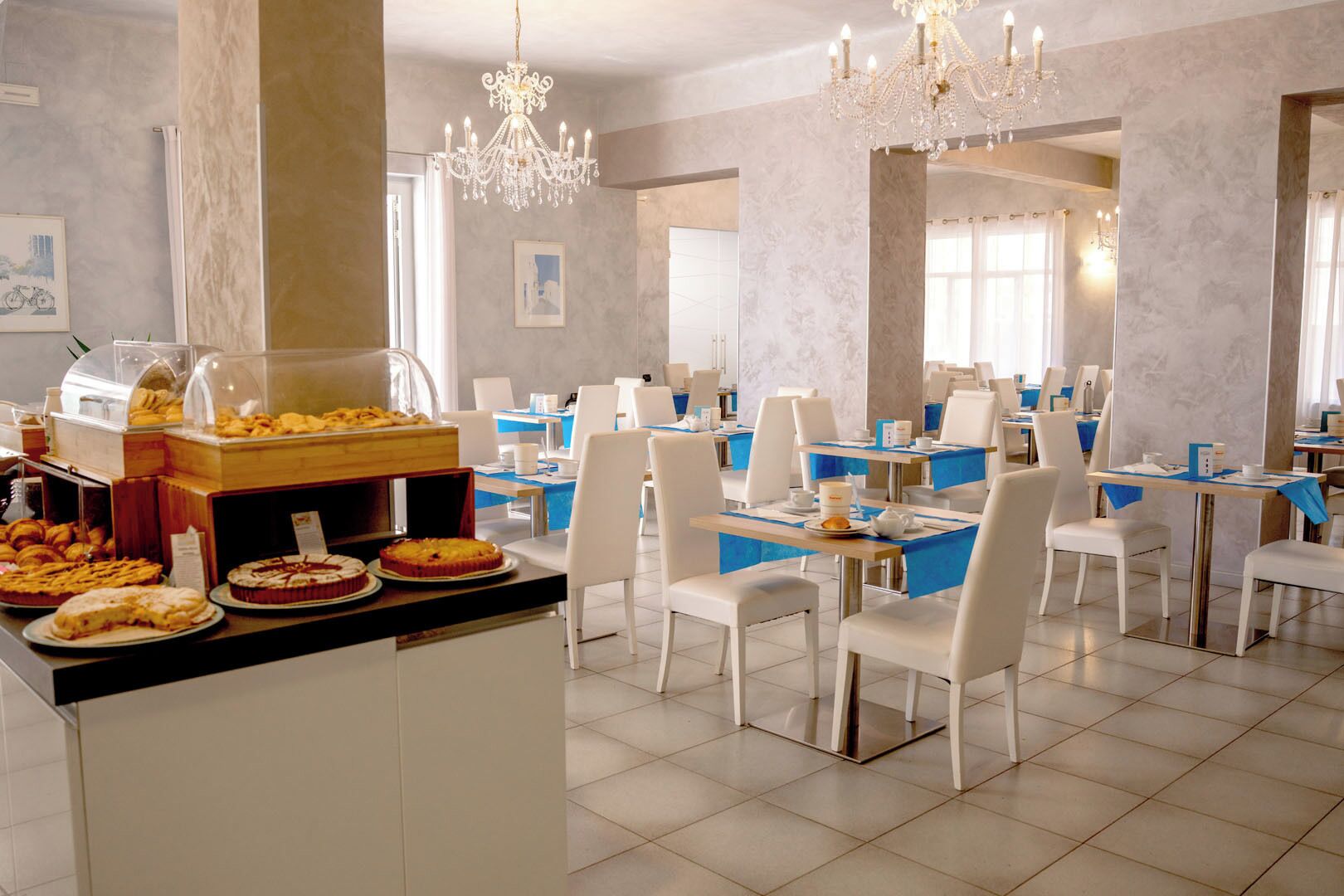 Comedor de hotel con varias mesas y sillas, un bufé con distintos tipos de comida y candelabros decorativos.