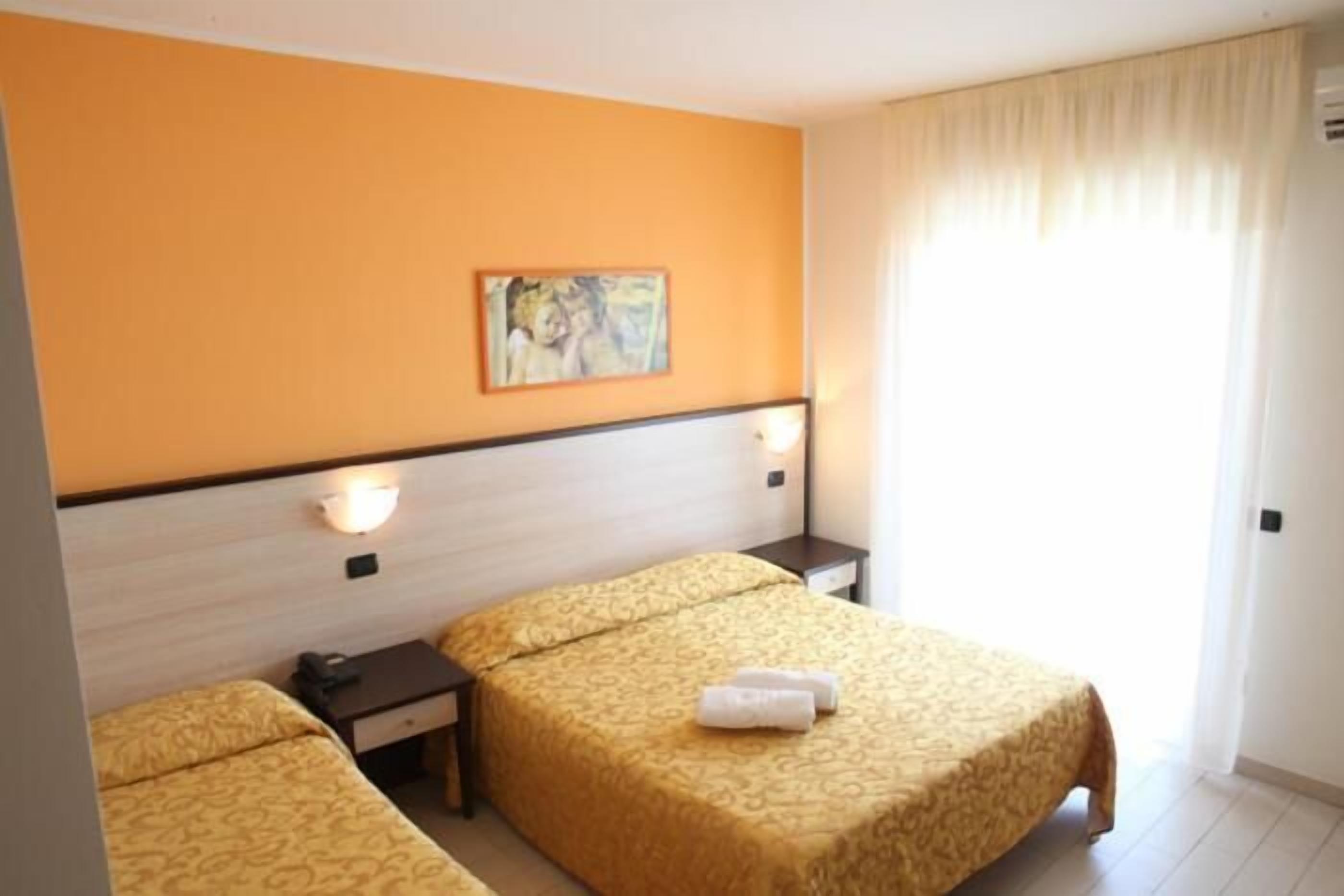 A hotel room with two beds, a painting on the wall, and a window with curtains.