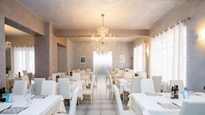 Un comedor de hotel con varias mesas y sillas, una araña y amplias ventanas.