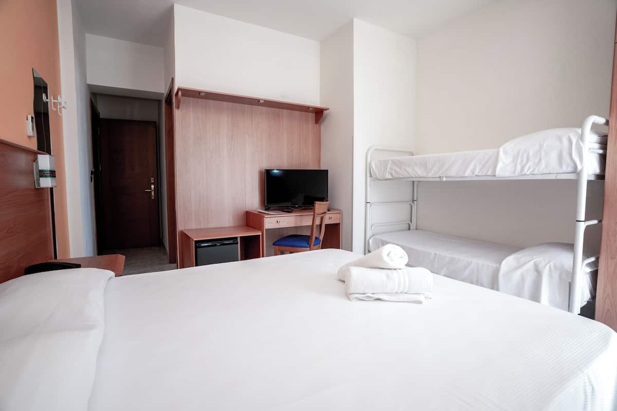Una habitación de hotel con cama, escritorio con televisor, litera y armario.