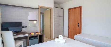 A hotel room with a bed, a desk with a TV, a chair, a small fridge, and a wooden door.