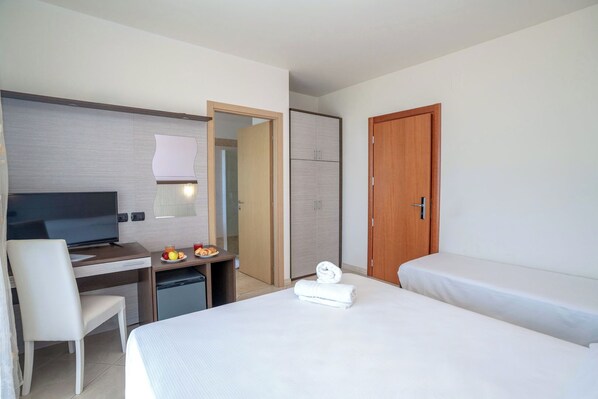 A hotel room with a bed, a desk with a TV, a chair, a small fridge, and a wooden door. - hotel Cristall (San Benedetto del Tronto)
