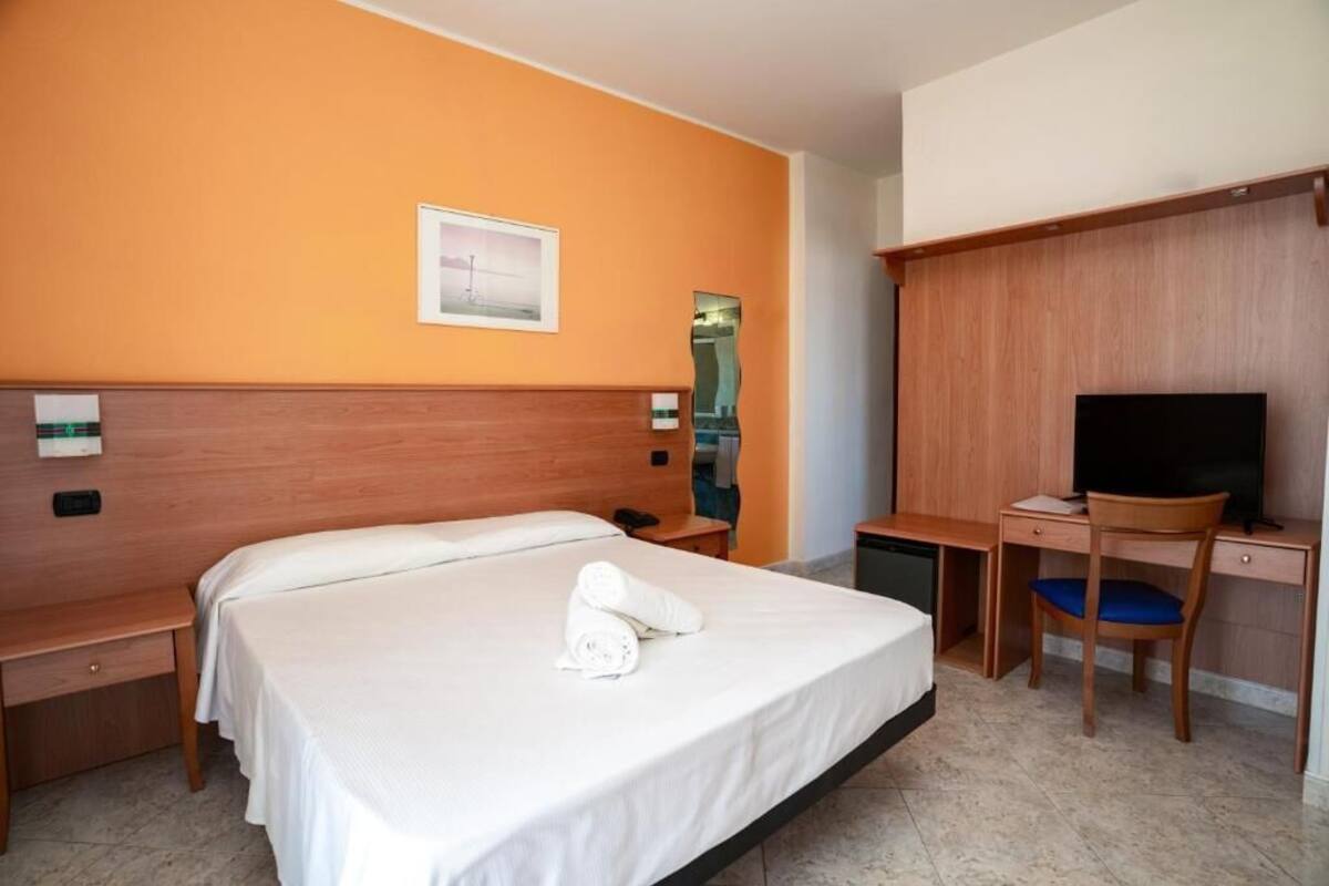 Una habitación de hotel con una cama, un escritorio, una silla, un televisor y un espejo.