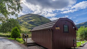 A wooden cabin with a sign reading "Florian," a wooden deck, and a gravel path leading to it. - Cosy Eco Cabin with stunning views (Glencoe)