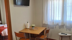 A room with a wooden dining table, four chairs, a TV mounted on the wall, a window with sheer curtains, and a small side table with a remote control. - Apartment near Padrón and Camino Portugués 5 (Pontecesures)