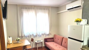 A compact living space with a wooden dining table, a pink sofa, a small white side table, and a white refrigerator. - Apartment near Padrón and Camino Portugués 5 (Pontecesures)