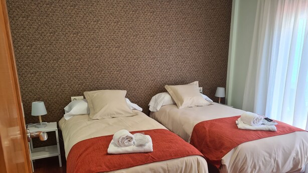 A hotel room with two beds, each with a red blanket and white pillows, a wooden floor, and a patterned wall. - Apartment near Padrón and Camino Portugués 5 (Pontecesures)