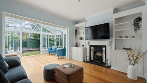 A spacious living room with a large TV, a fireplace, and a conservatory with glass doors. - Relaxed Family Retreat in Kingston (Greater London)