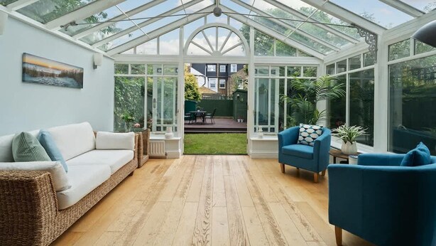 A conservatory with a glass roof, wicker furniture, and potted plants. - Relaxed Family Retreat in Kingston (Greater London)