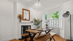A dining area with a wooden table and benches, a fireplace, and a large window with a view of greenery. - Relaxed Family Retreat in Kingston (Greater London)